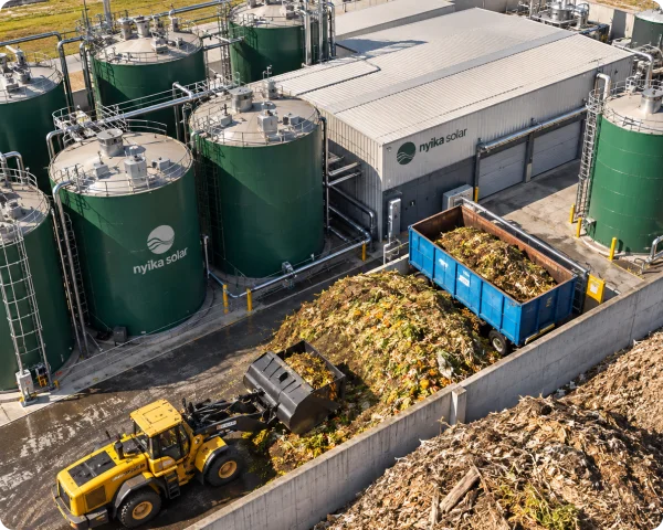Organic food and agricultural waste fed by an inclined conveyor into a Nyika Solar-branded processing facility with stainless steel tanks.