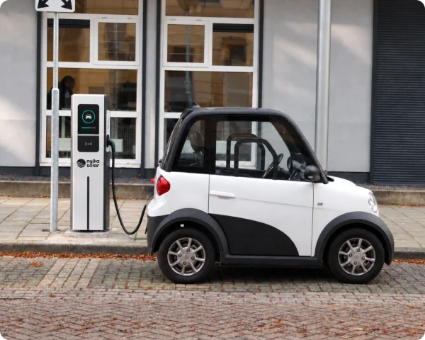 Compact electric city car connected to a Nyika Solar freestanding AC charging pedestal beside an urban building.